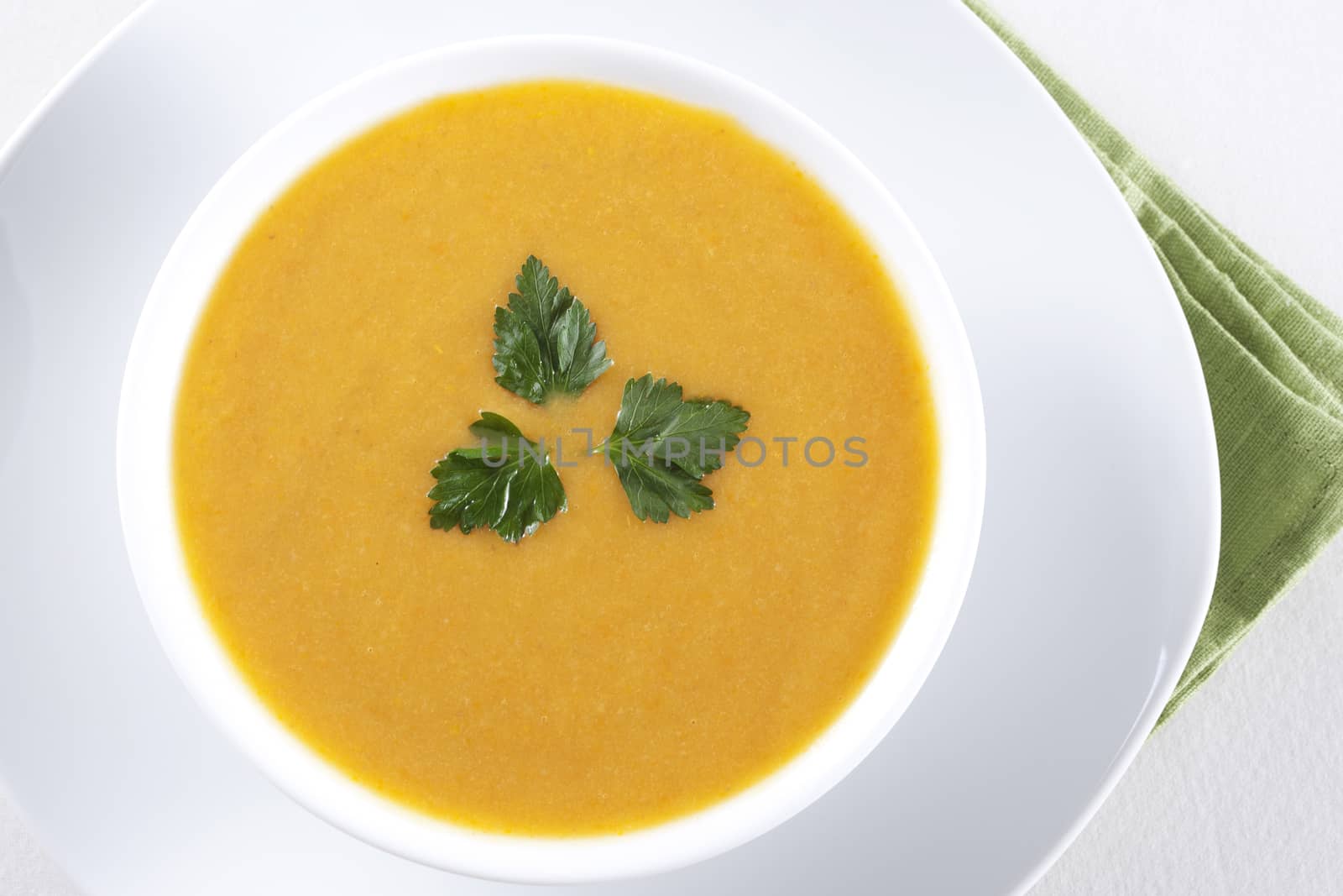 A bowl of yellow soup with parsley 