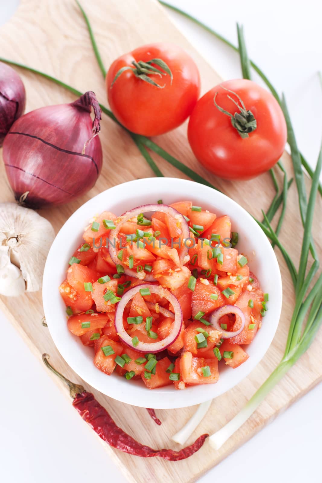 Salsa in a bowl on a wooden board and the ingredients: tomatoes, onions, garlic, chili pepper