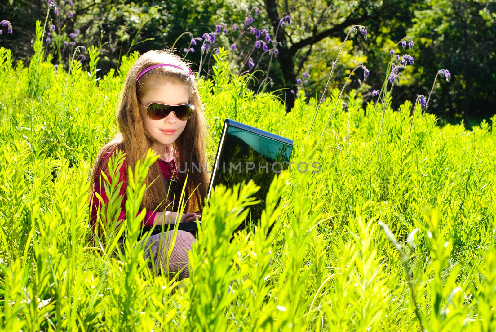 Smiling little girl with laptop outdoor. Sunny summer day.