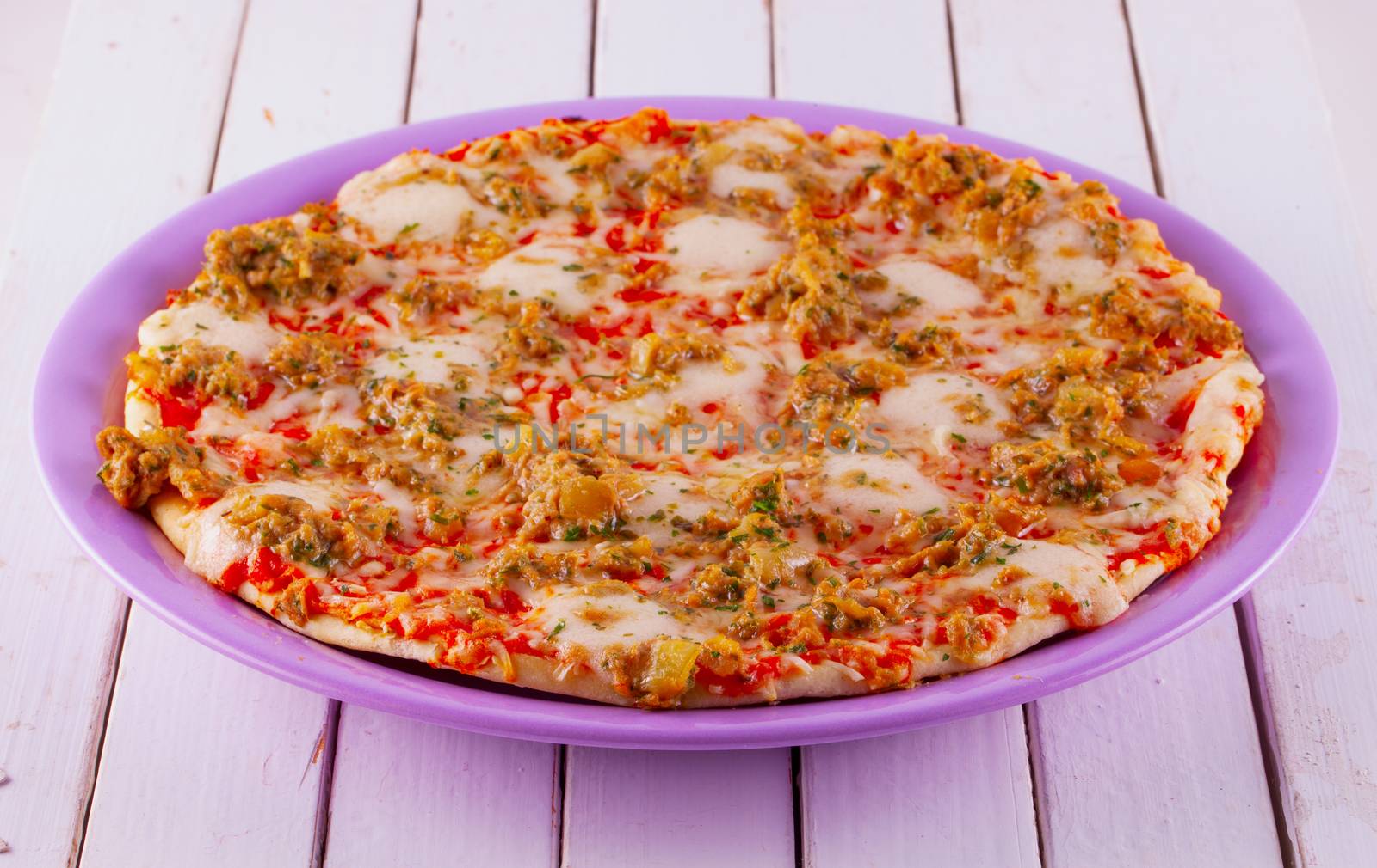 Entire view of pizza over purple plate, white wooden table