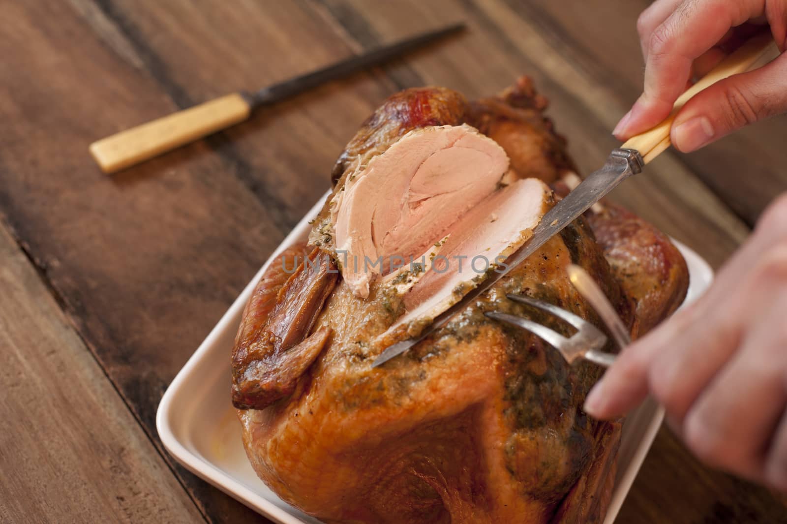 Overhead view of the hands of a man carving a roast turkey with a carving knife and fork slicing the breast meat ready for a Thanksgiving or Christmas dinner