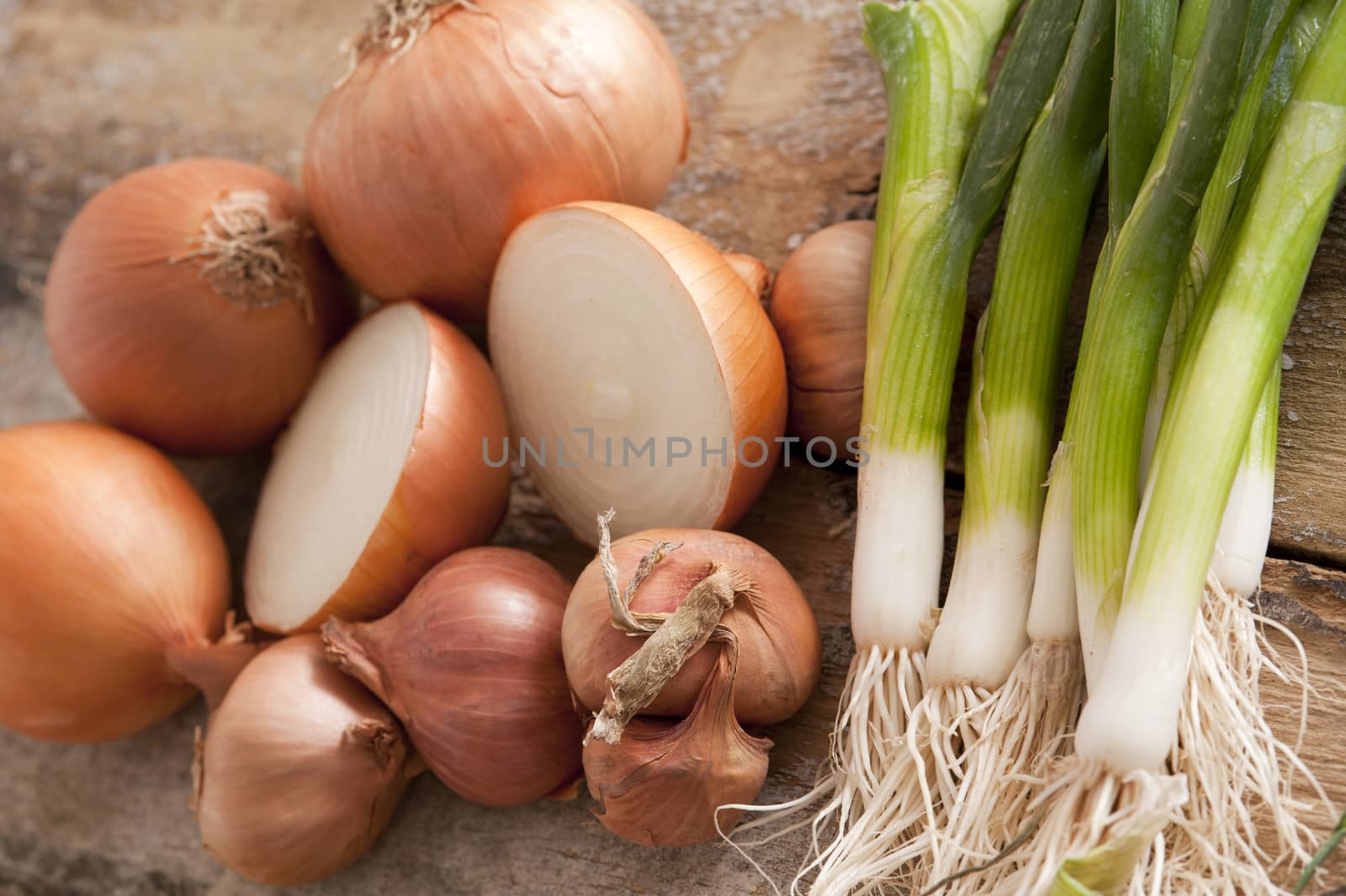 Fresh whole and halved brown onions with a bunch of young scallions to be used as a pungent flavoring in cooking or salads, close up overhead background view