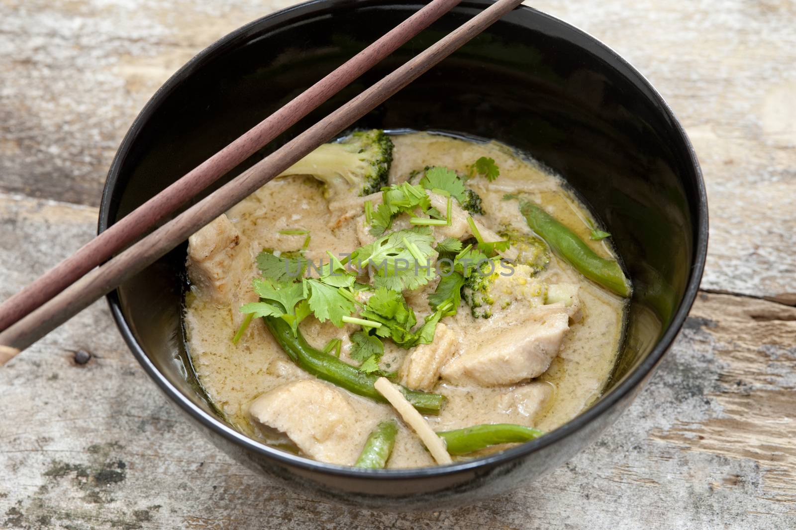 Bowl of delicious healthy creamy Thai green curry with diced chicken pieces served with chopsticks, high angle view
