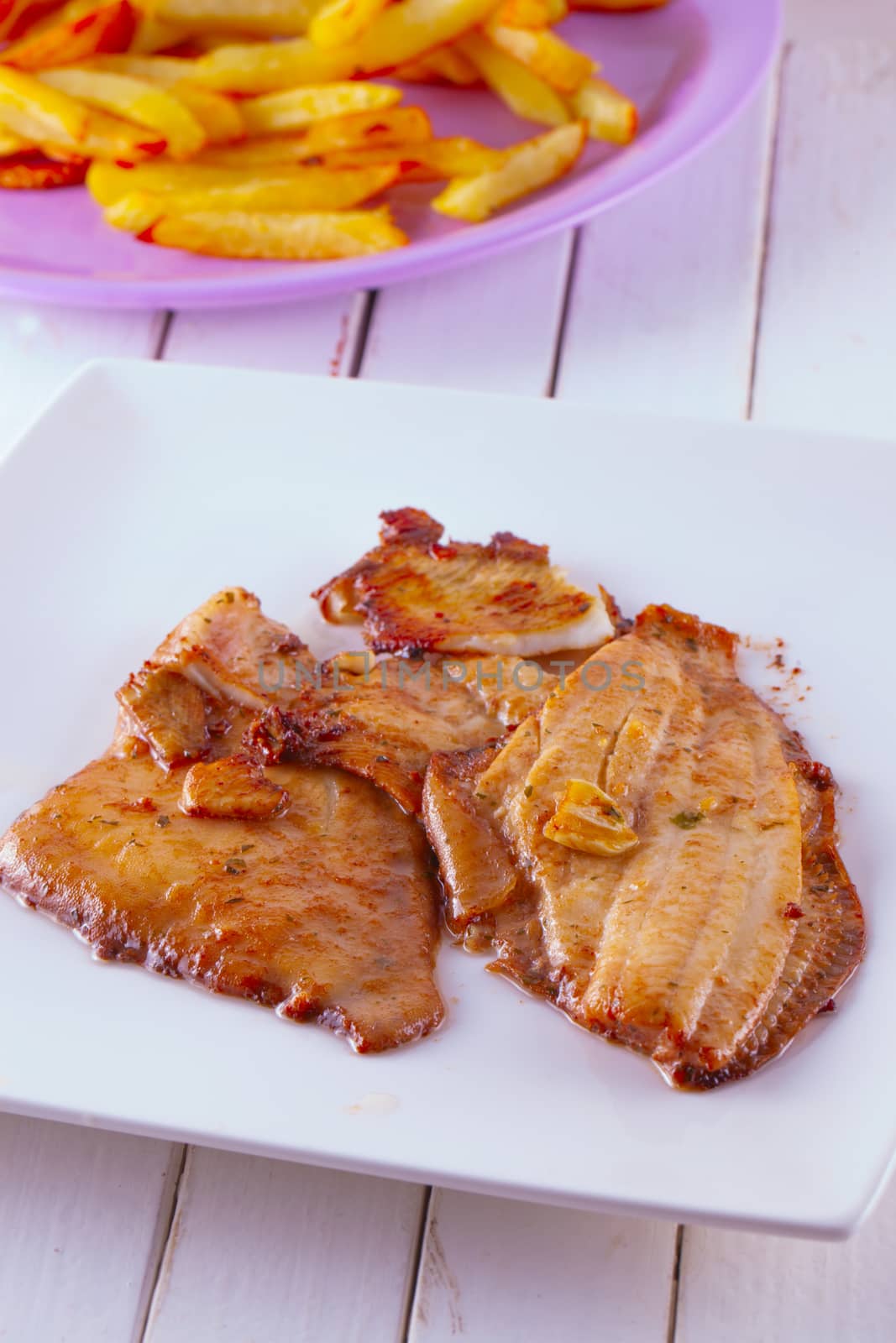 Hake in a white plate with fried potatoes on the back