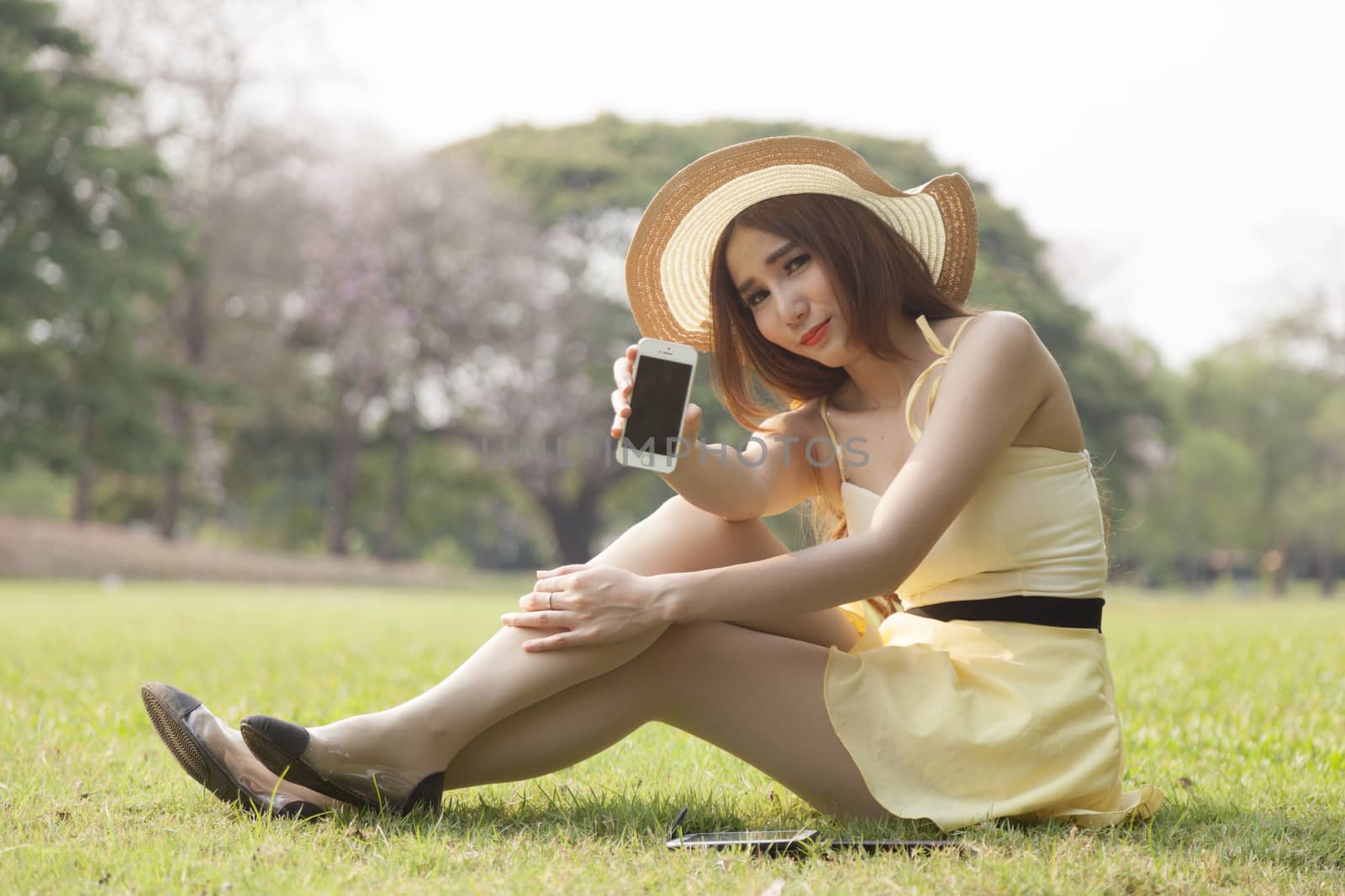 Woman filing phone. Sitting on the grass in the park.
