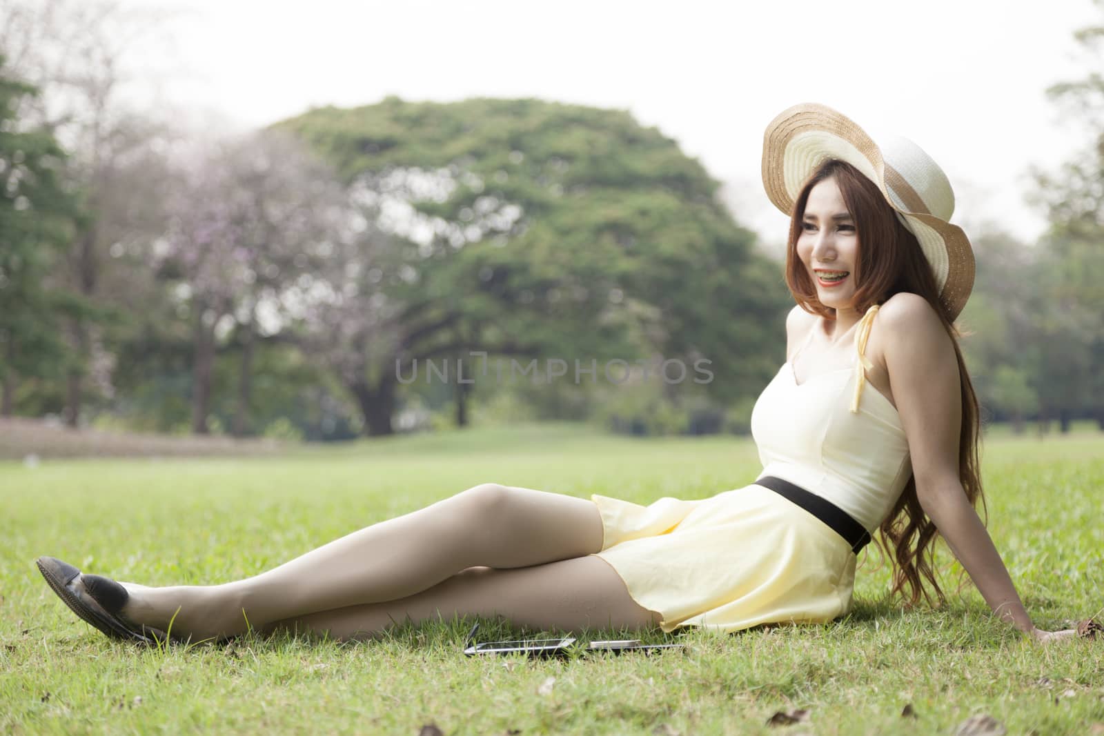 Relaxing on the lawn. Woman wearing hat sitting and relaxing on the grass in the park.