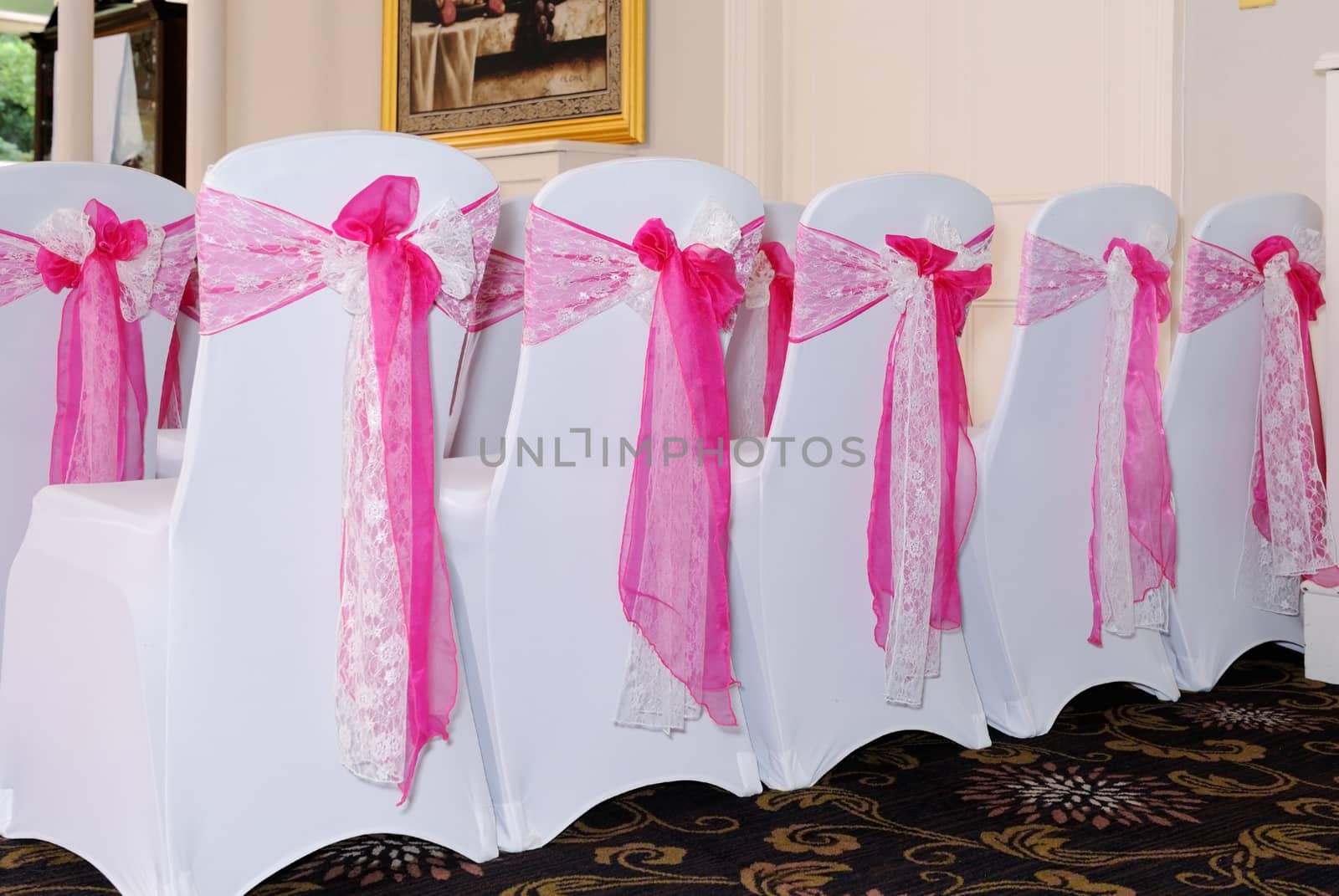 Wedding ceremony with chairs covered in pink and white linen and with bow