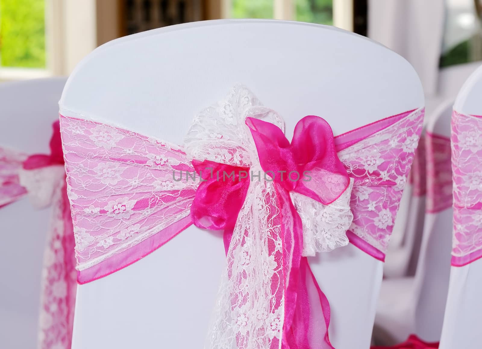 Pink and white chair cover at wedding ceremony showing ornate detail of bow and ribbon