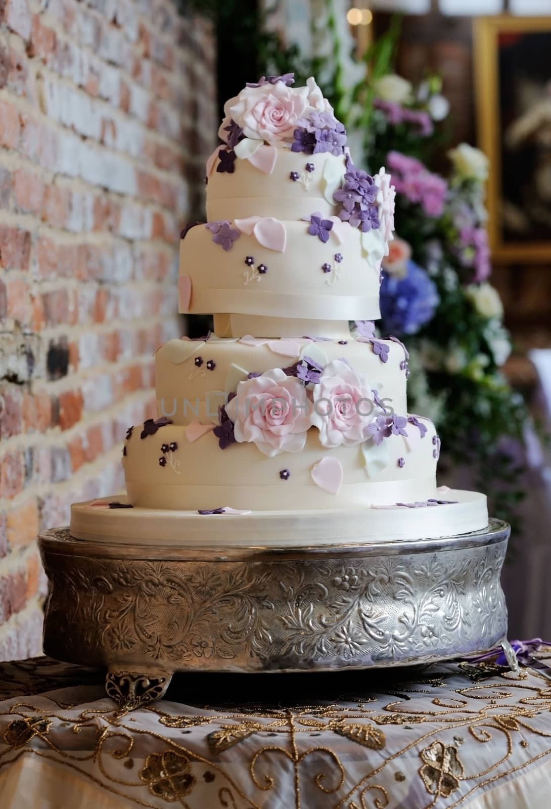 Wedding cake at reception has intricate decoration of pink and purple flowers