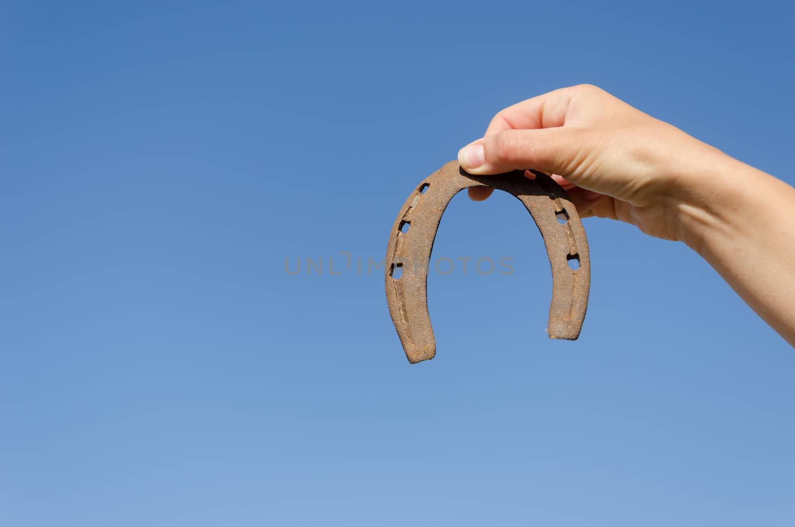 small rusty iron horseshoe in woman hand on blue sky bckground