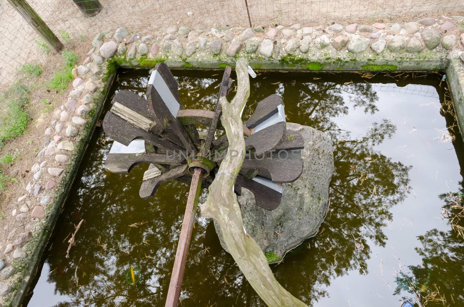 stylized small wooden water mill on the stone base of the park pond