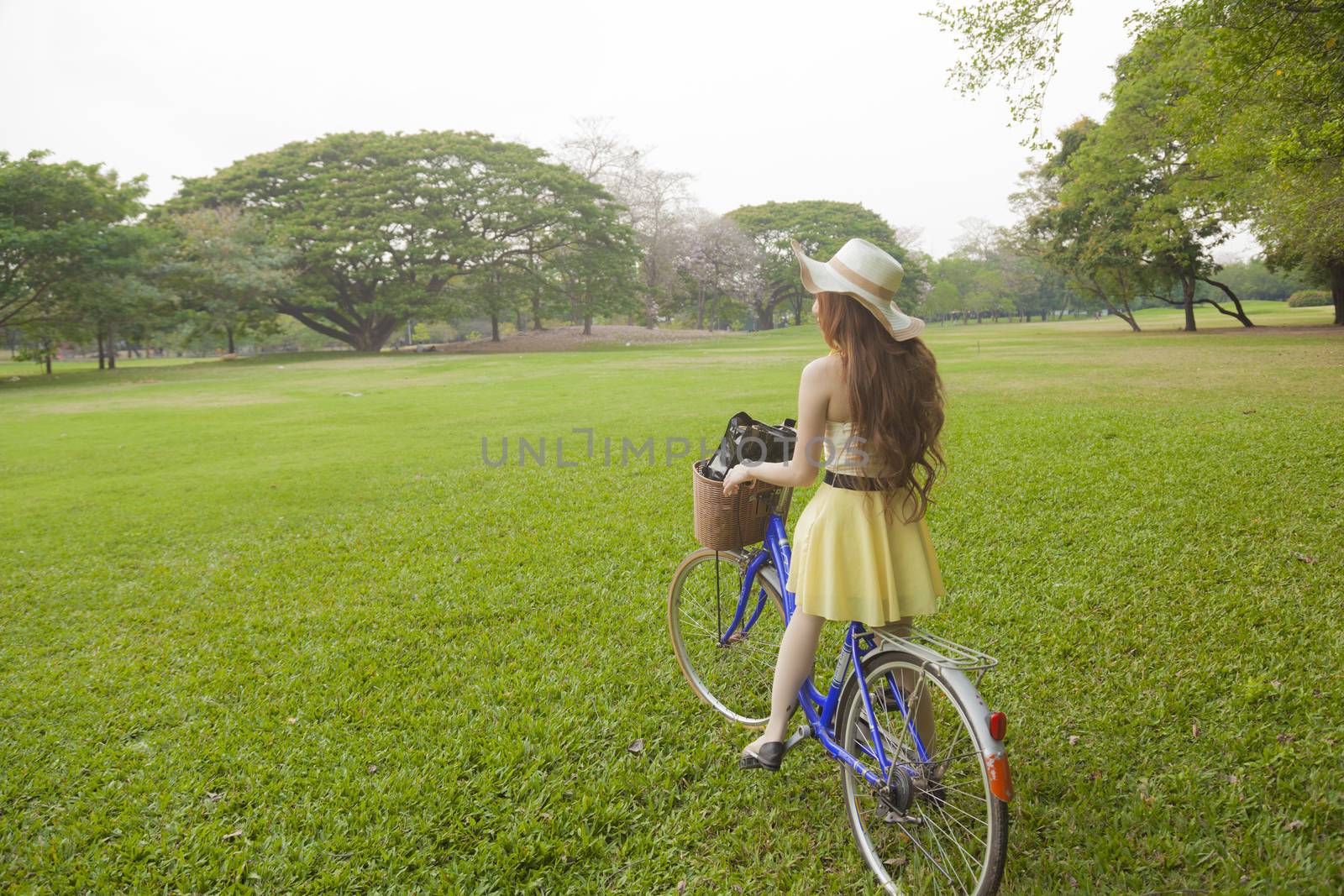 Woman riding a bicycle. Woman with hat riding a bicycle in the park.