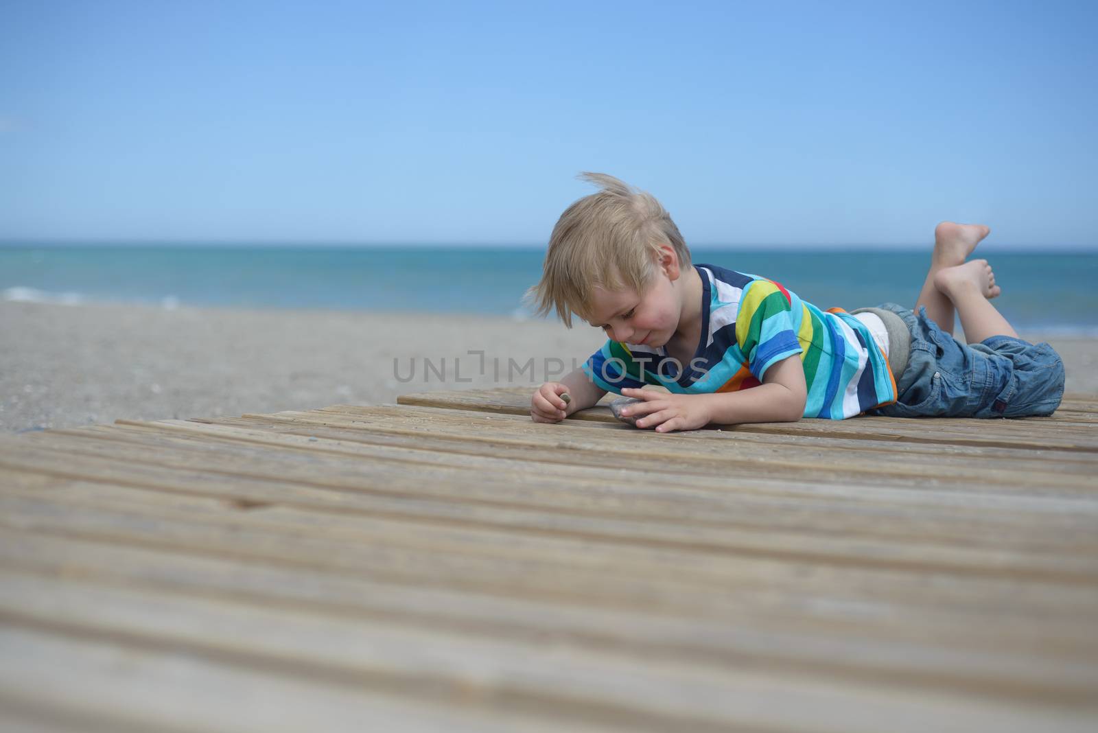 Small boy laying down on a wooden walkway on the beach