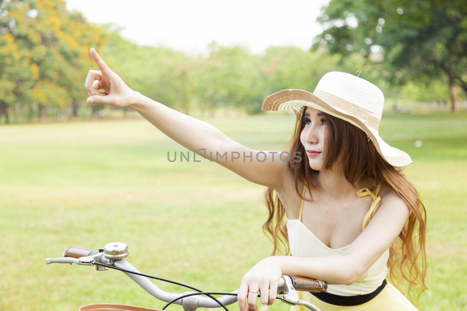 Woman sitting on the bike and pointing forward. In the lawn of the park.