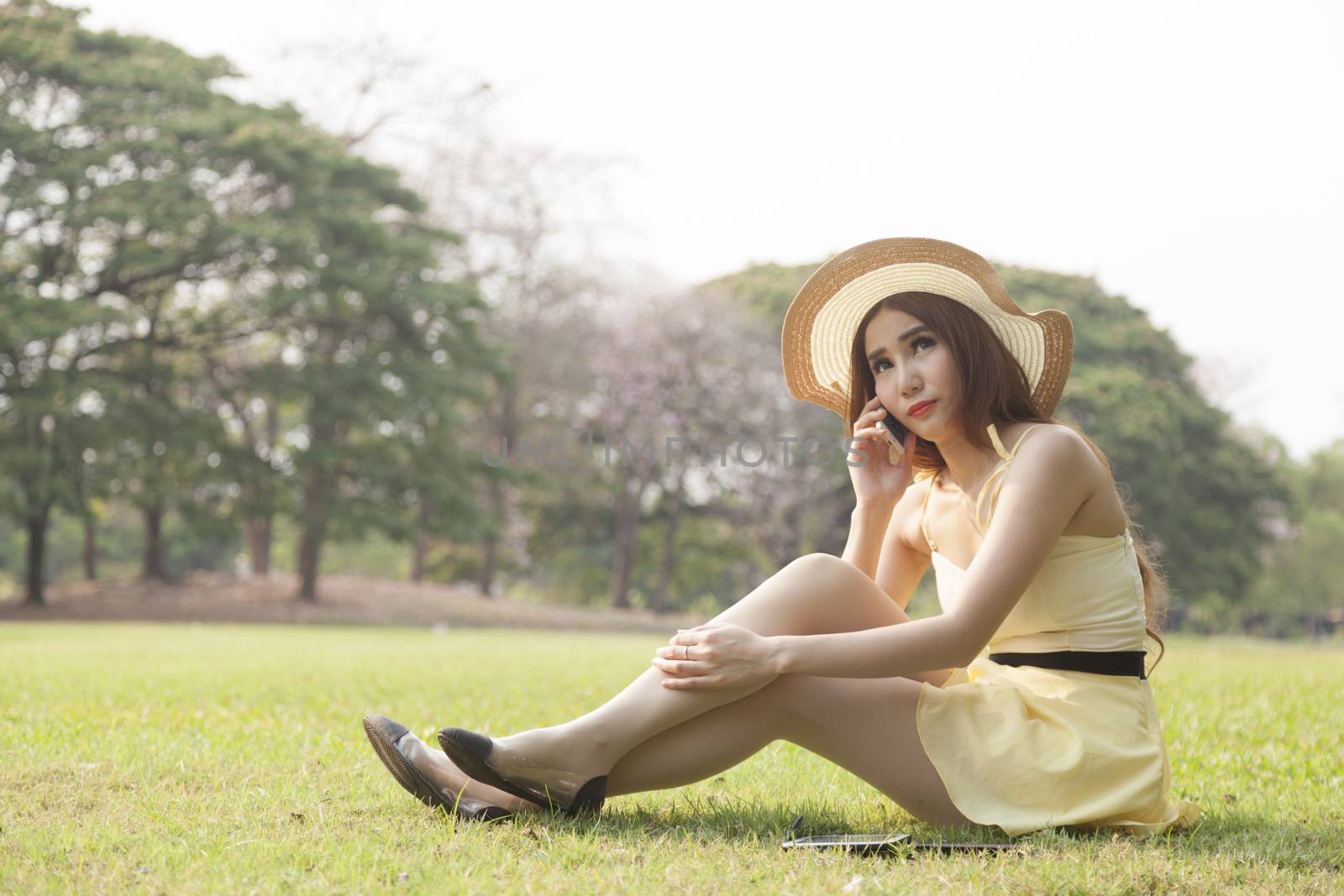 Woman sitting and talking on phone. Sitting on the grass in the park.