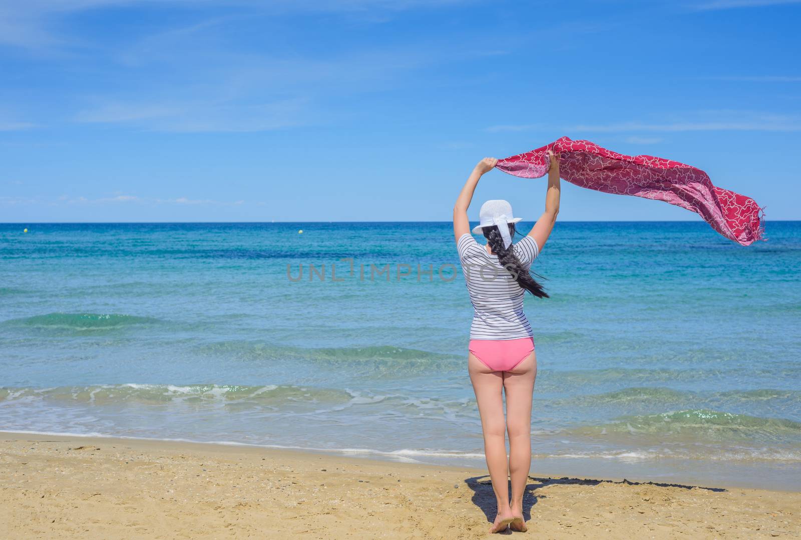 Young woman holding a red fabric on windy beach
