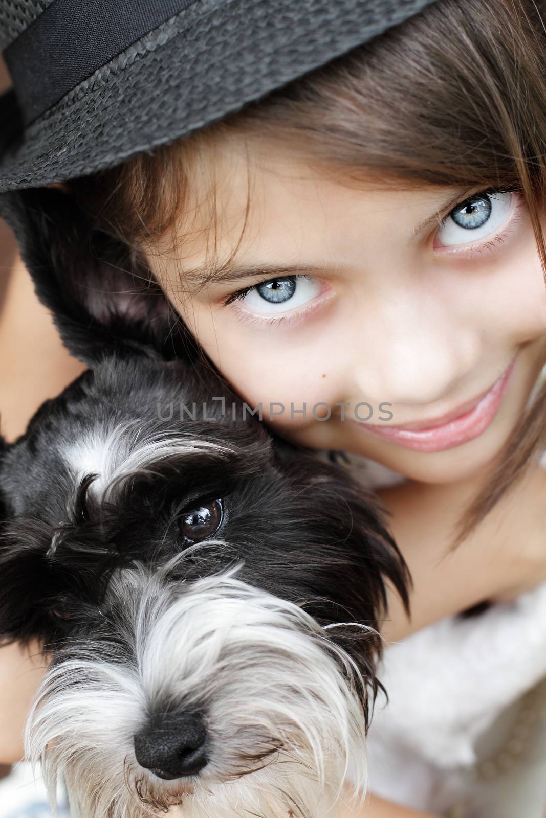 Young girl looking directly into the camera, wearing a fashionable black hat and snuggling her puppy. Extreme shallow depth of field with selective focus on eyes.