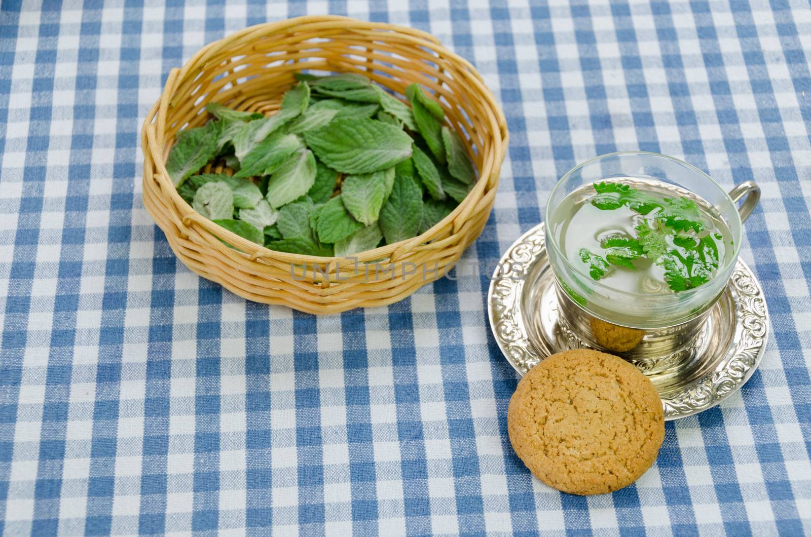 fresh healthy mint tea prepared in cup and dietary oatmeal cookie on checkered tablecloth