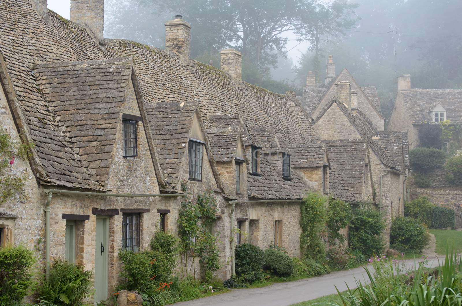 The Arlington Row, honey coloured weavers cottages in the morning fog in the town of Bibury in Gloucestershire in the Cotswolds, England, UK. The houses were built in 1380. 