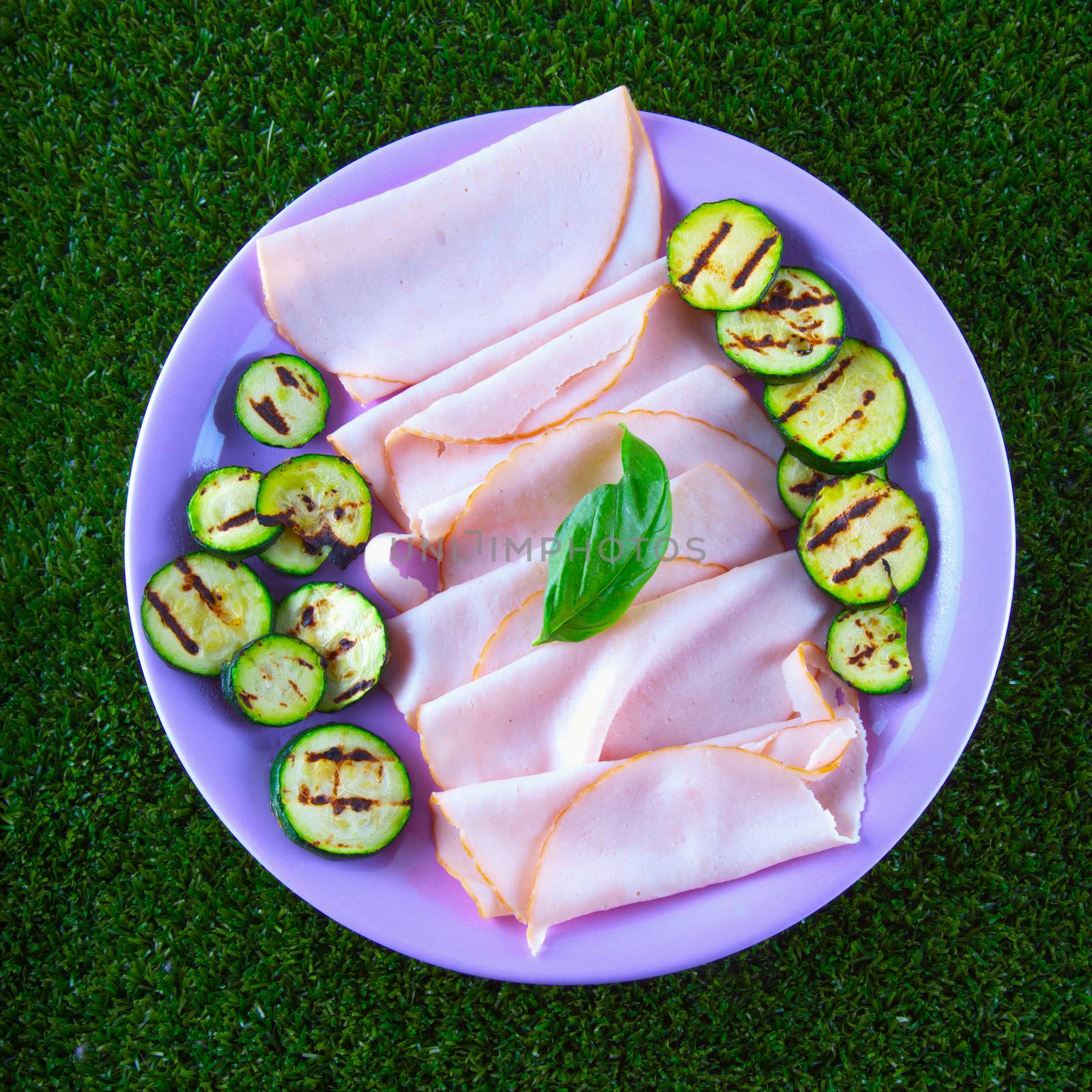 Turkey ham with grilled zucchini in a purple plate, over grass