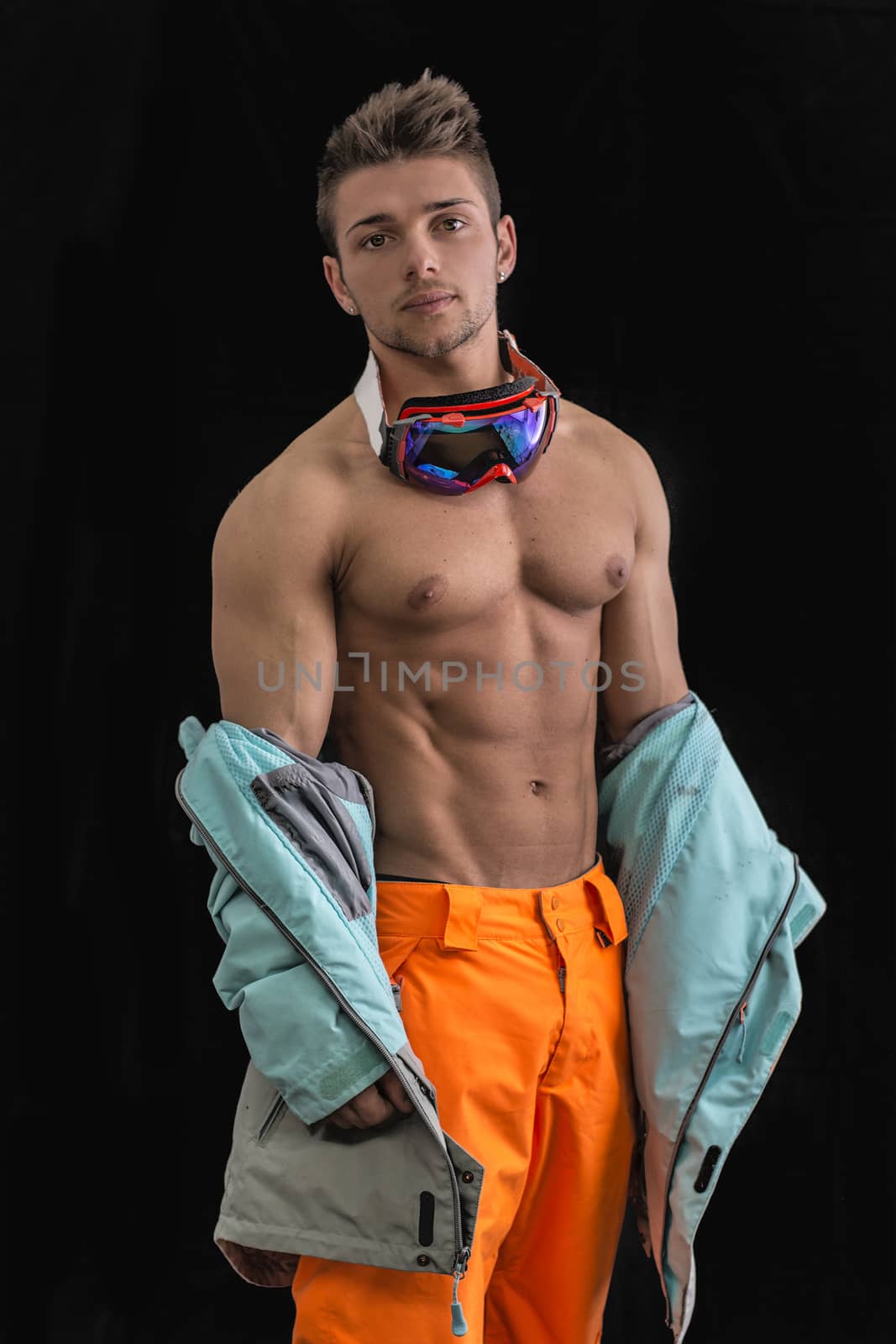 Attractive young male skier or snowboarder taking off jacket on naked muscular torso