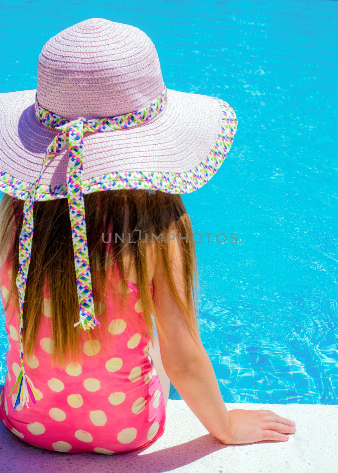 Young girl sat by the pool with a large sun hat on ,lots of copy space and room for text 