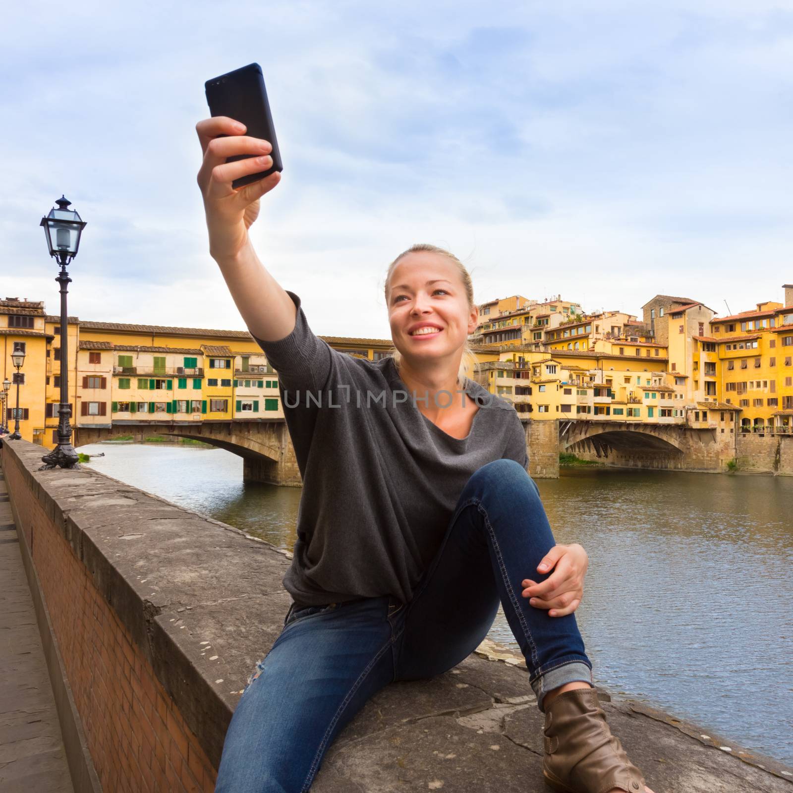 Young lady taking selfie in front of Ponte Vecchio bridge in Florence, Tuscany, Italy, during her summer vacations in Europe.