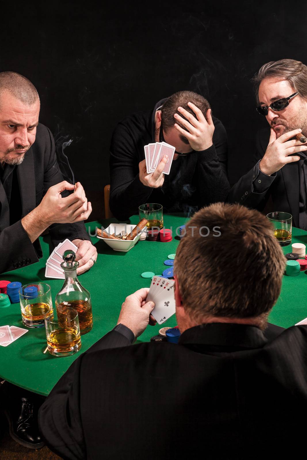 Photo of men playing poker, drinking and smoking, and looking uncertain of their luck.