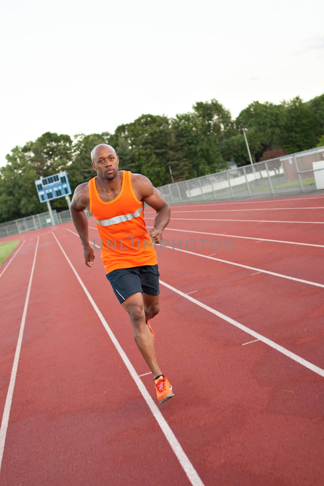 African American man in his 30s running at a sports track outdoors.