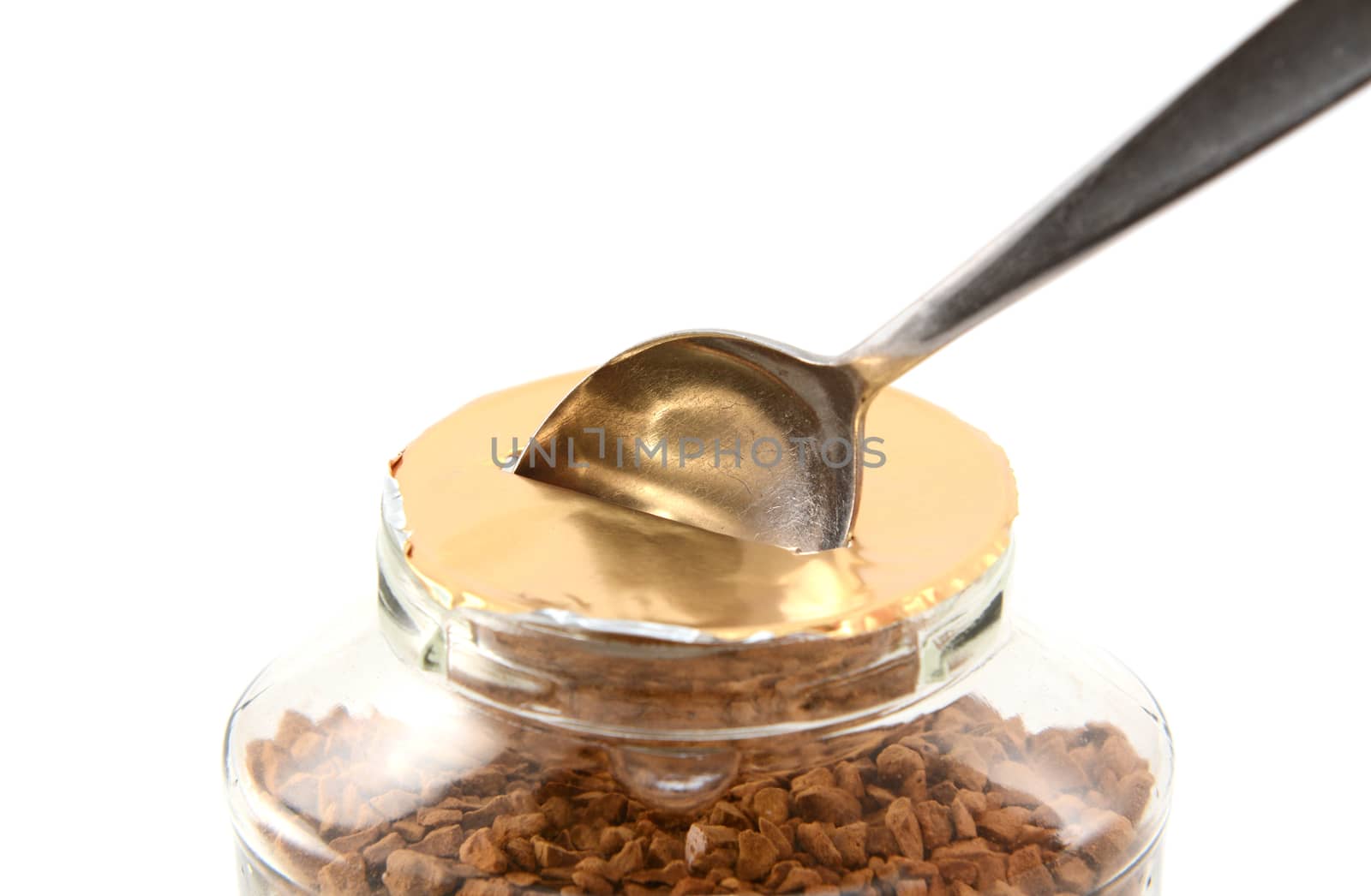 Metal teaspoon breaking the foil seal on a jar of instant coffee granules for the first time, isolated on a white background