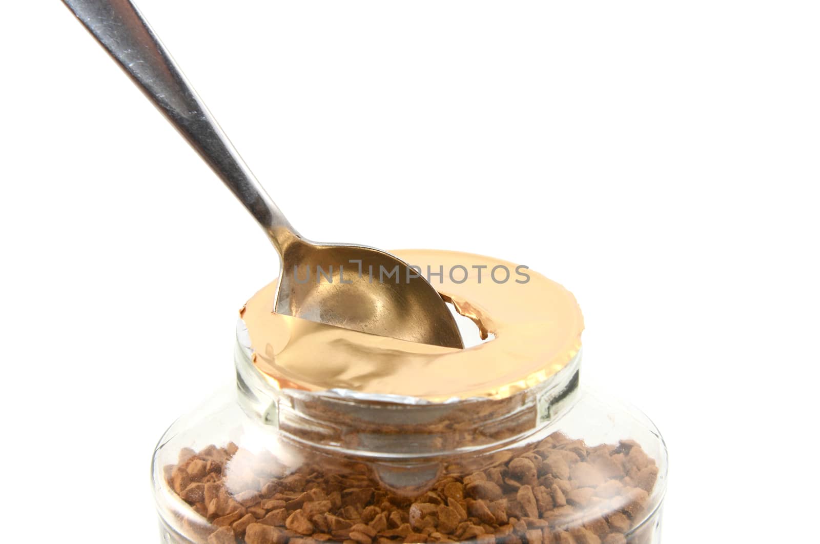 Ripping a hole in the foil of a new jar of instant coffee granules with a teaspoon, isolated on a white background