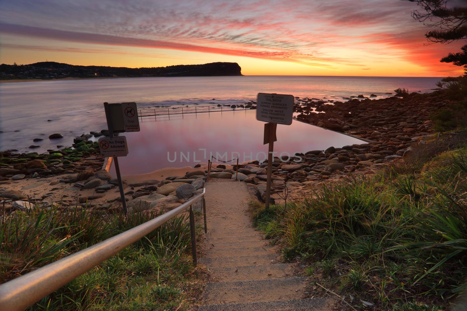 Low tide exposes the rocky end of Macmasters Beach where the tidal pool is calm reflecting pretty patterns in the sunrise sky