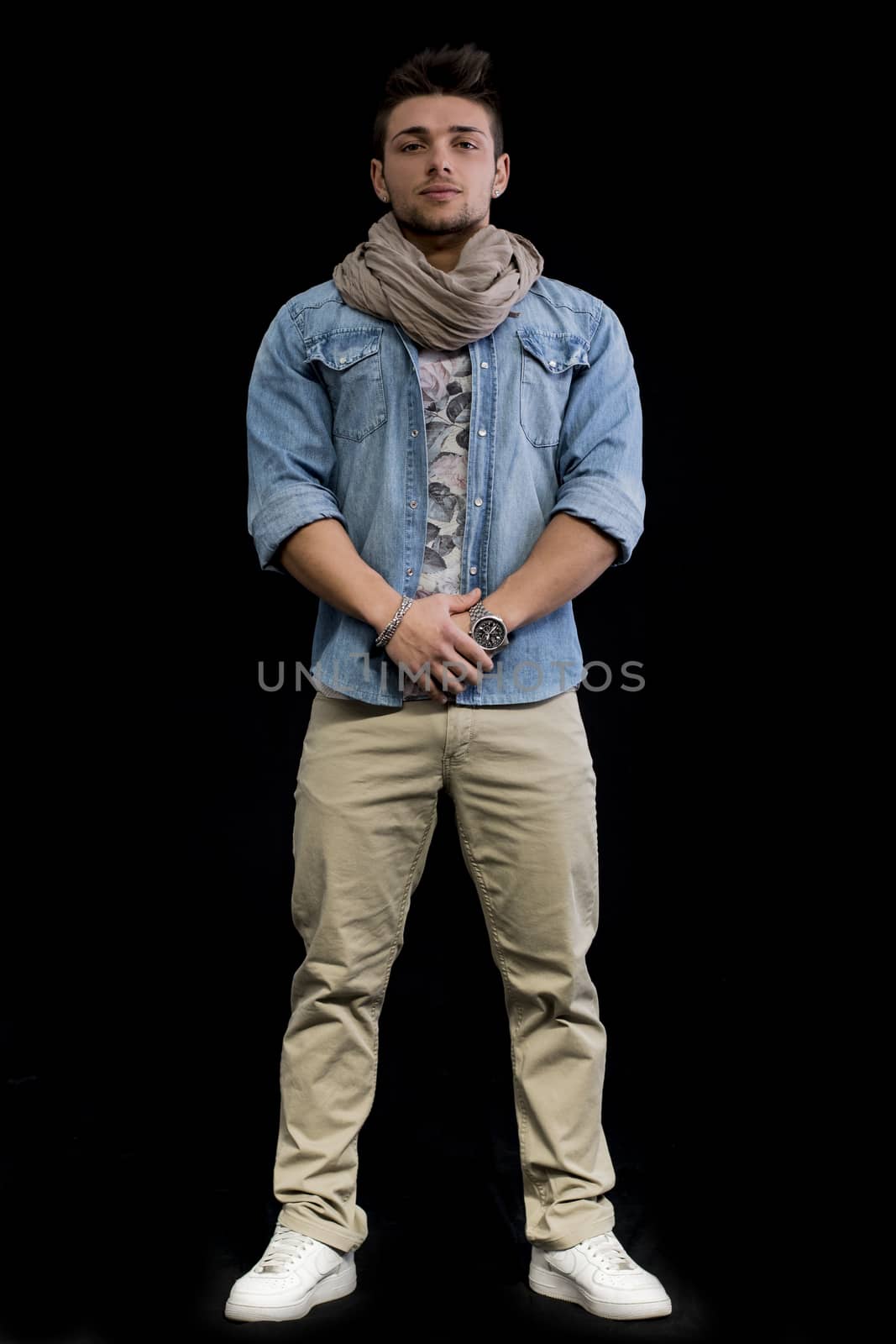 Full length body shot of attractive young man standing on black background, looking at camera
