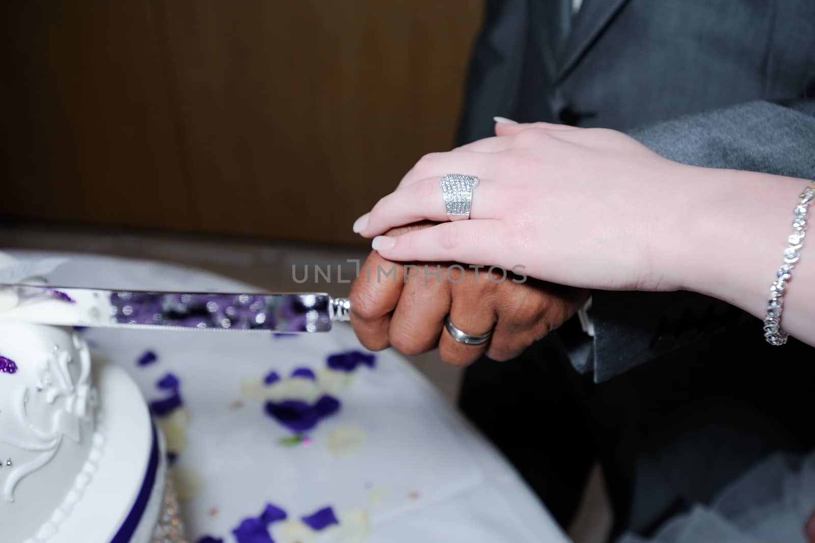 Bride and groom on wedding day cutting cake closeup showing rings and knife