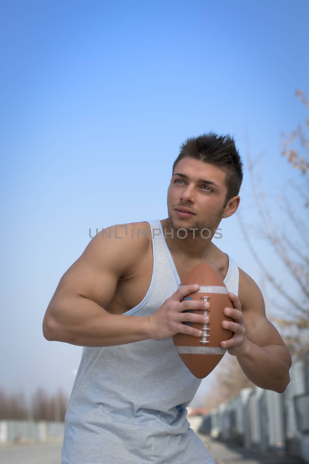 Muscular american football player ready to throw ball in hand. Outdoors shot