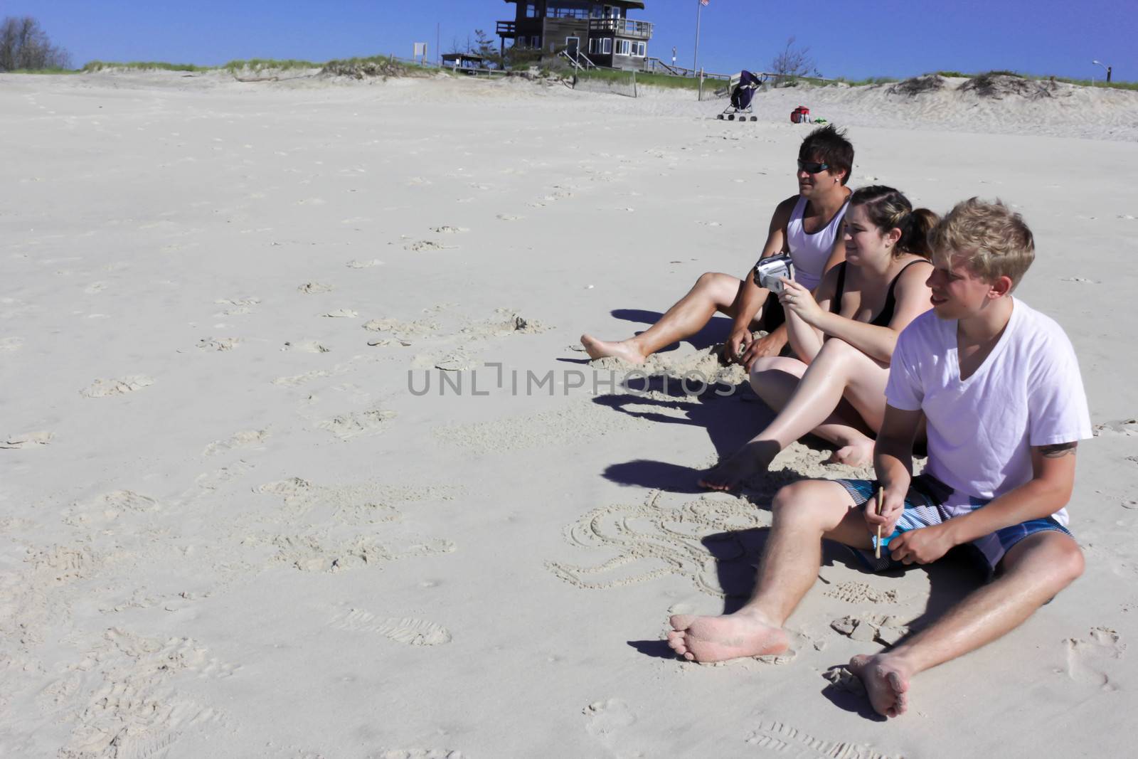 family sitting on the beach while recording an event.