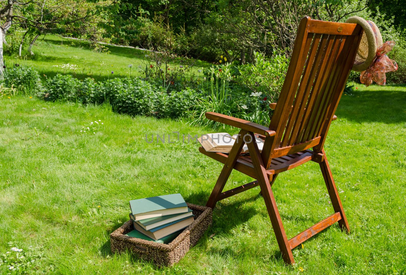 wooden relax chair, books in basket and hat in garden yard in summer day.
