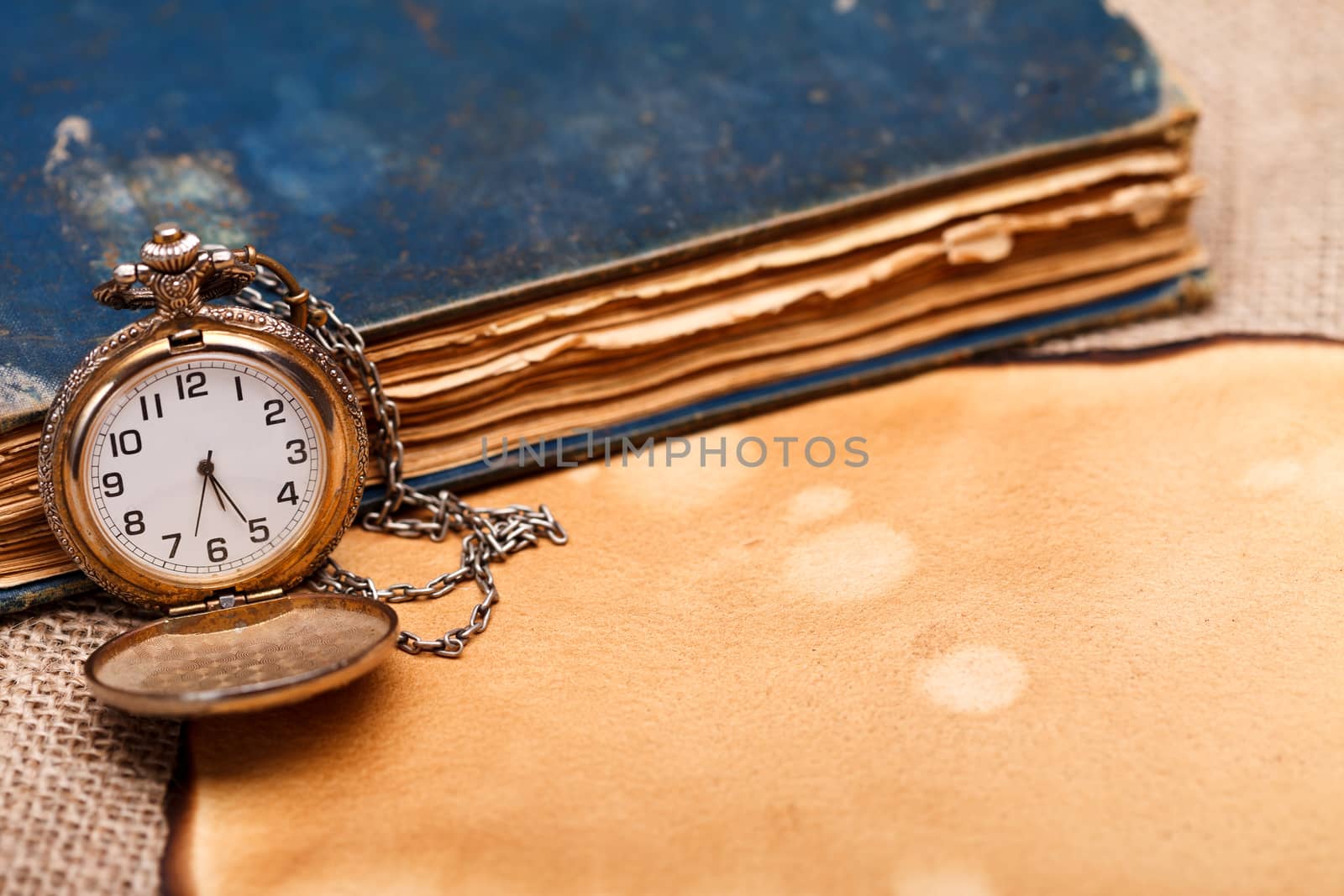 Old pocket watch with antique book and paper on burlap background.
