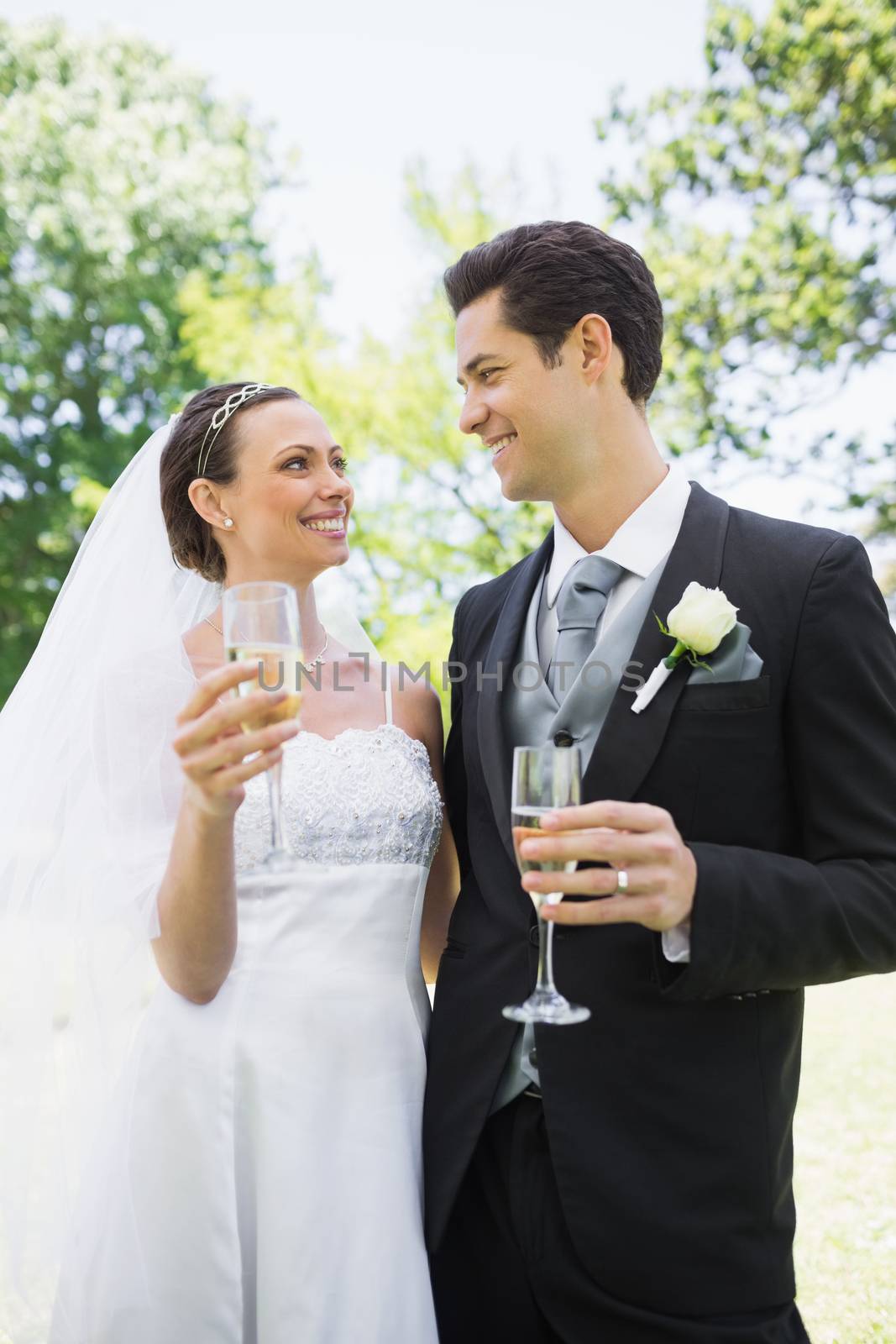 Romantic bride and groom having champagne while looking at each other in park