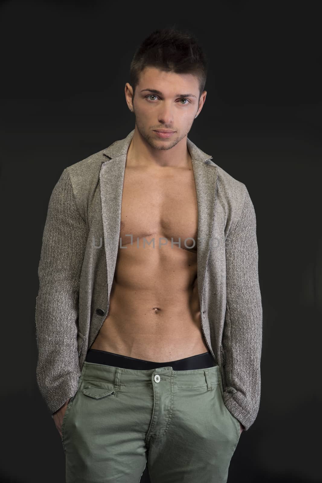 Confident, attractive young man with open jacket on muscular torso, ripped abs and pecs, hands in pockets