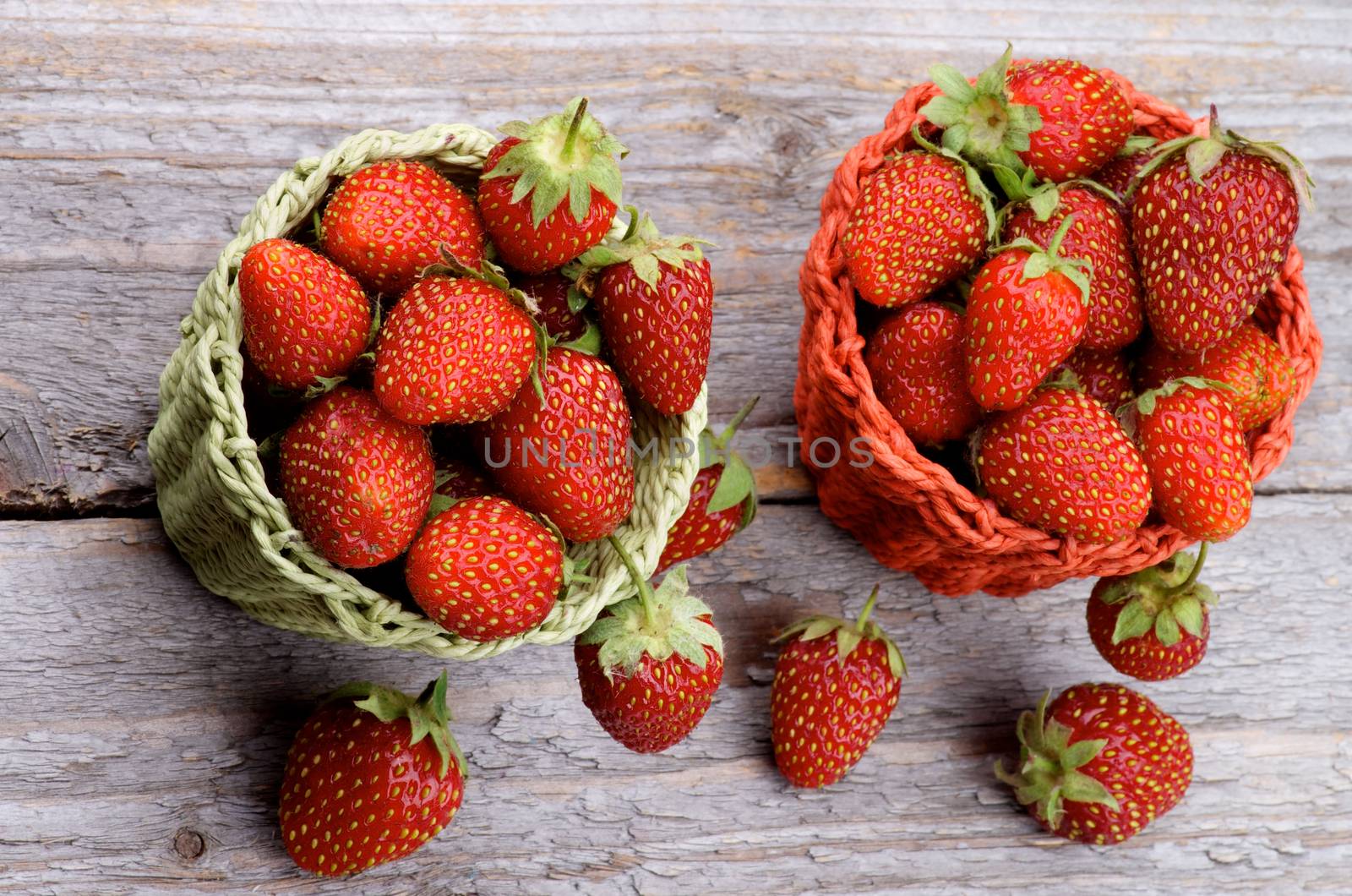 Forest Strawberries in Red and Green Wicker Baskets isolated on Rustic Wooden background. Top View