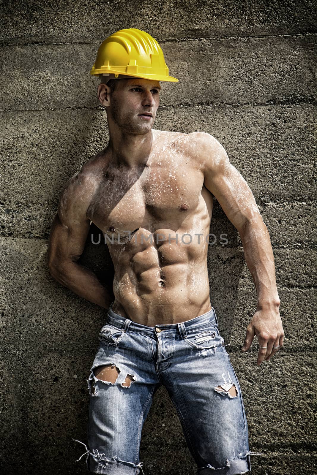 Handsome construction worker standing shirtless in front of a concrete wall