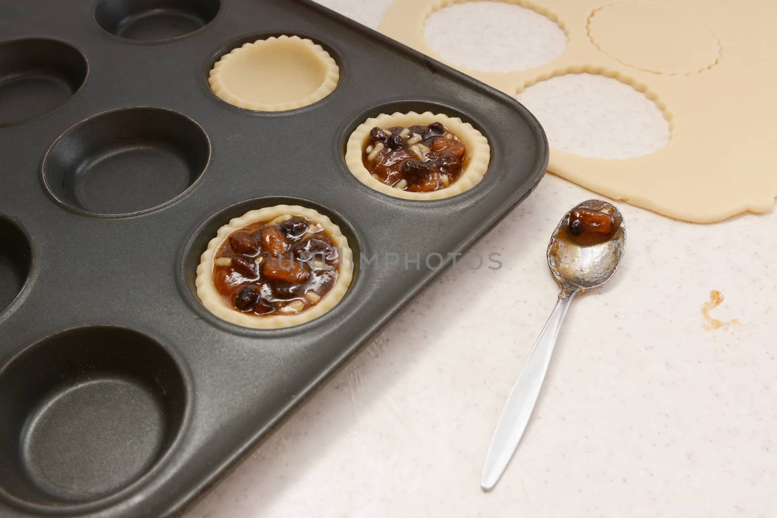 Filling pastry cases with mincemeat, with a used teaspoon on worktop