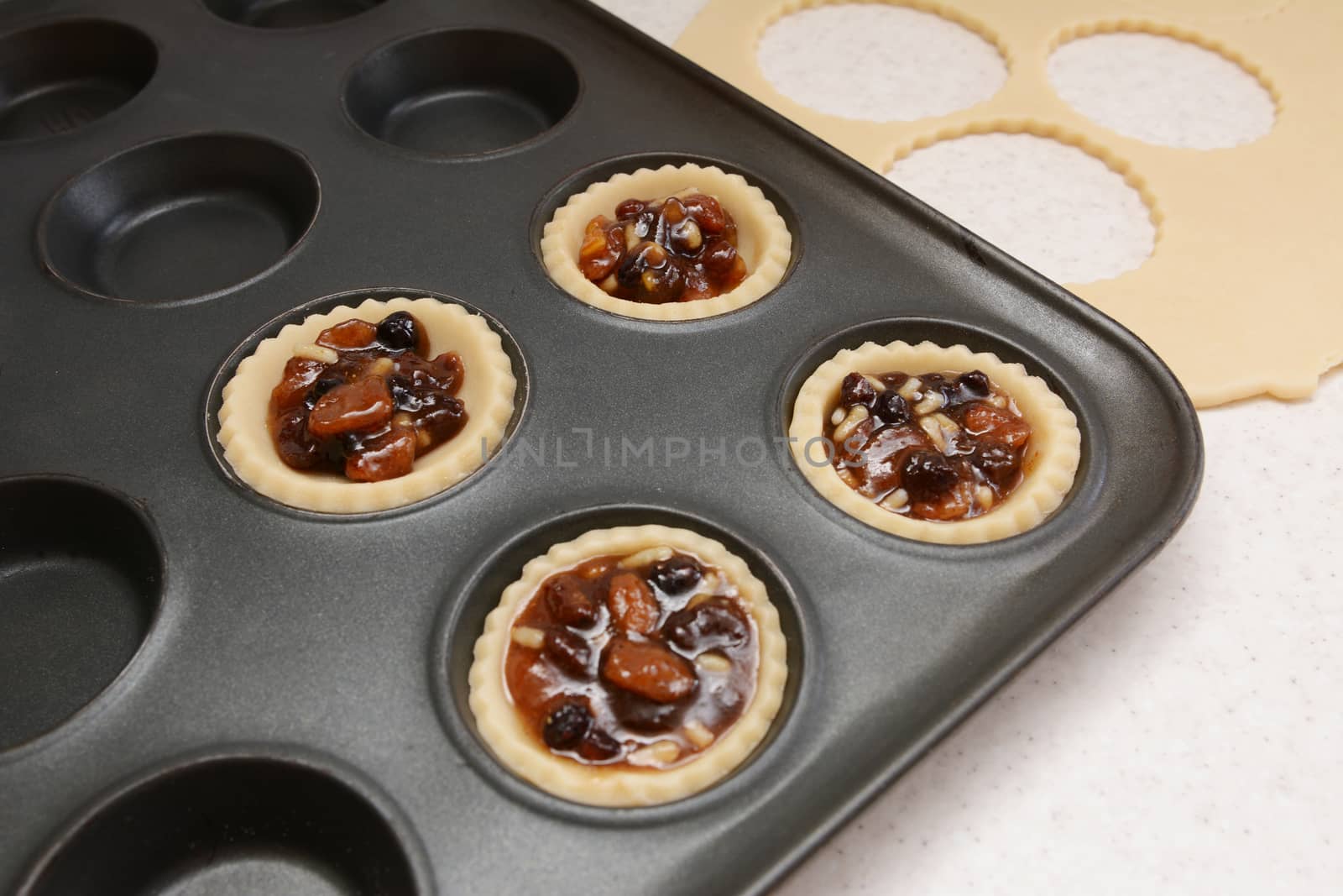 Producing mince pies; four pastry cases filled with mincemeat, dough scraps beyond