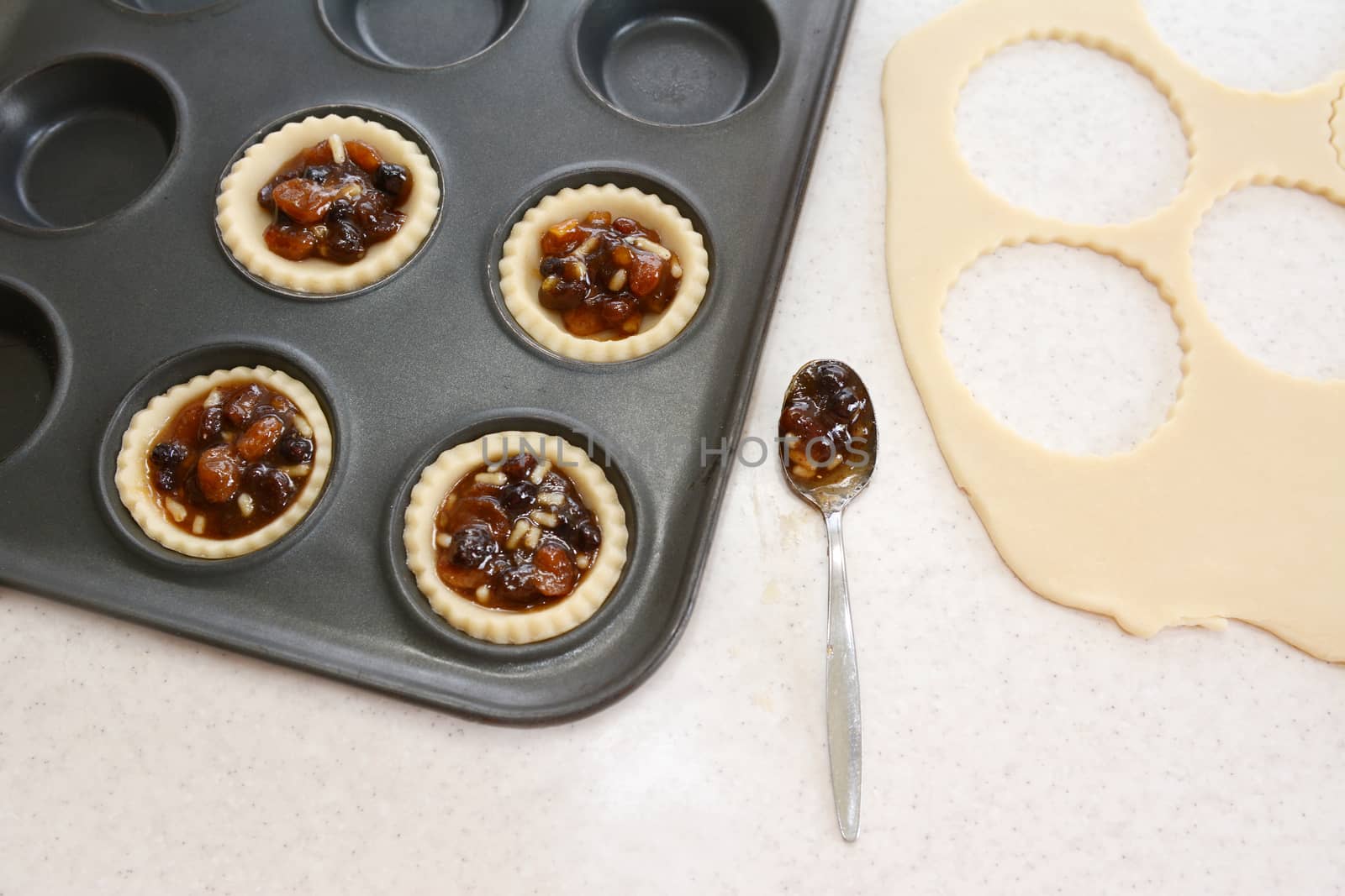 Making mince pies in the kitchen - filled pastry cases, mincemeat, dough scraps and teaspoon