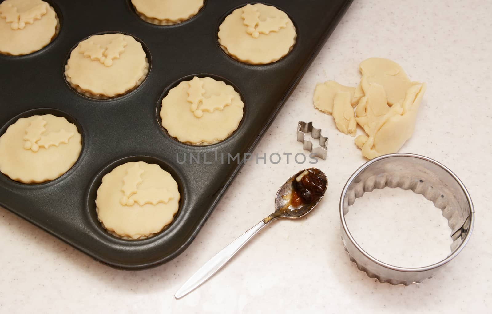 Uncooked mince pies in a bun tin, pastry leftovers, teaspoon and cutters