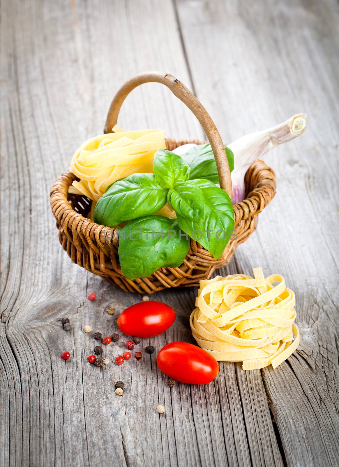 Italian pasta fettuccine nest with garlic, tomatoes and fresh basil leaves, on wooden background