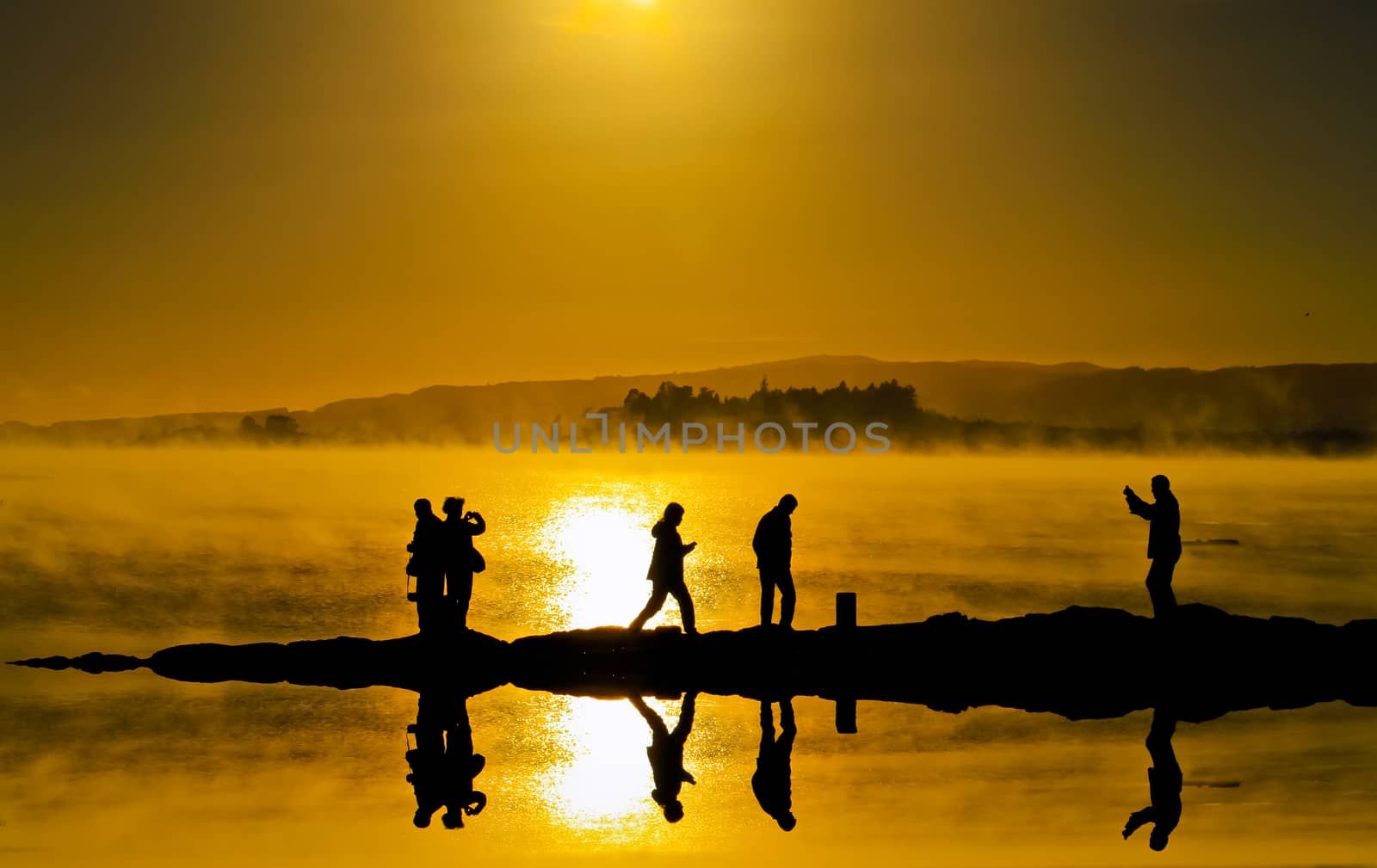 Silhouettes   and reflecting on water surface of people who are taking a walk and take photo at rotorua lake New zealand.