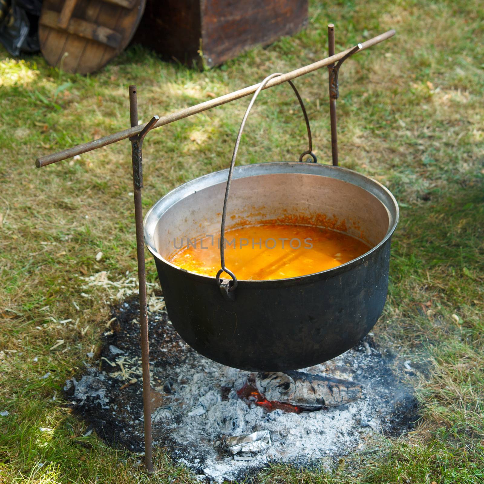 A black cauldron hanging on a campfire with soup in it