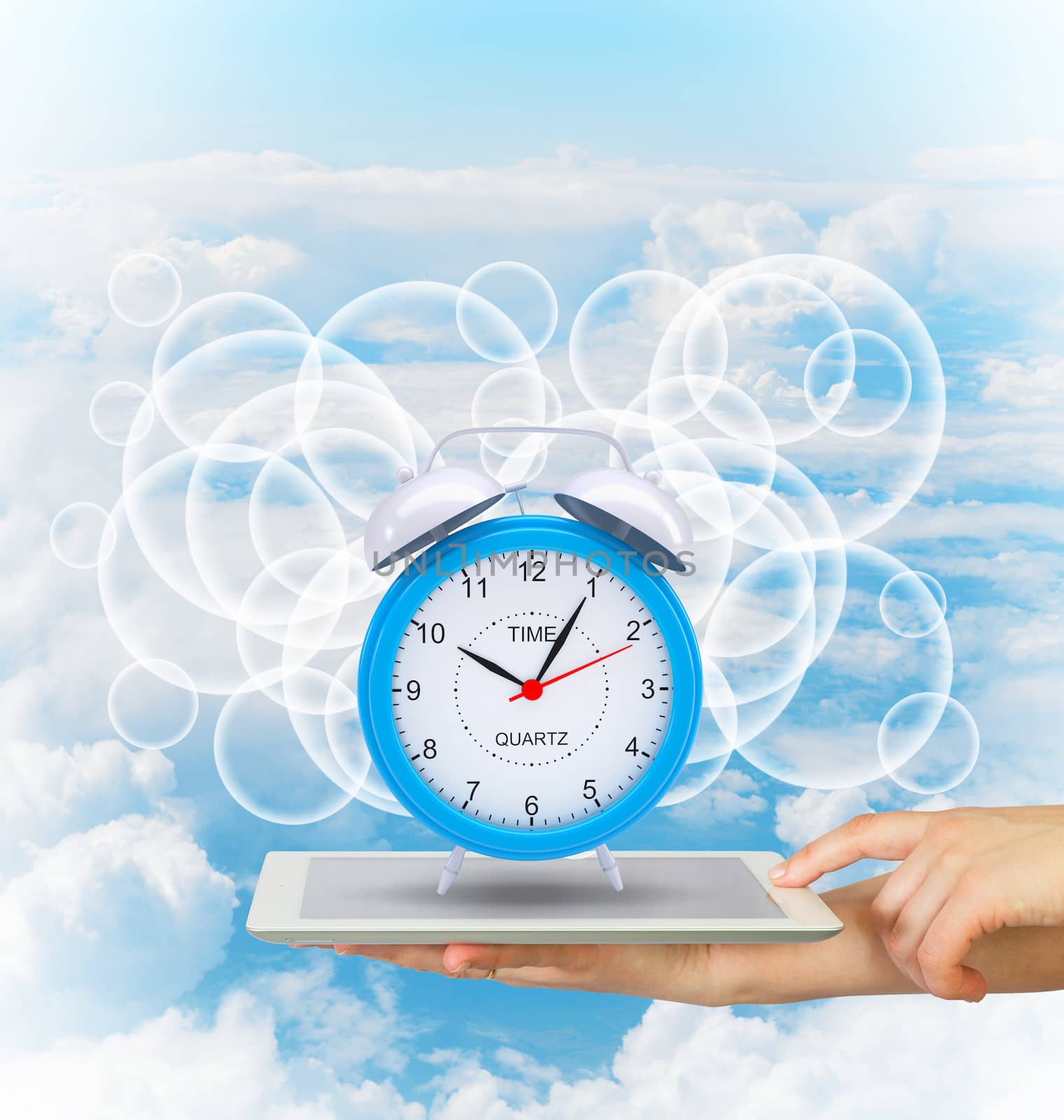 Hands hold tablet pc with alarm clock. Blue sky background